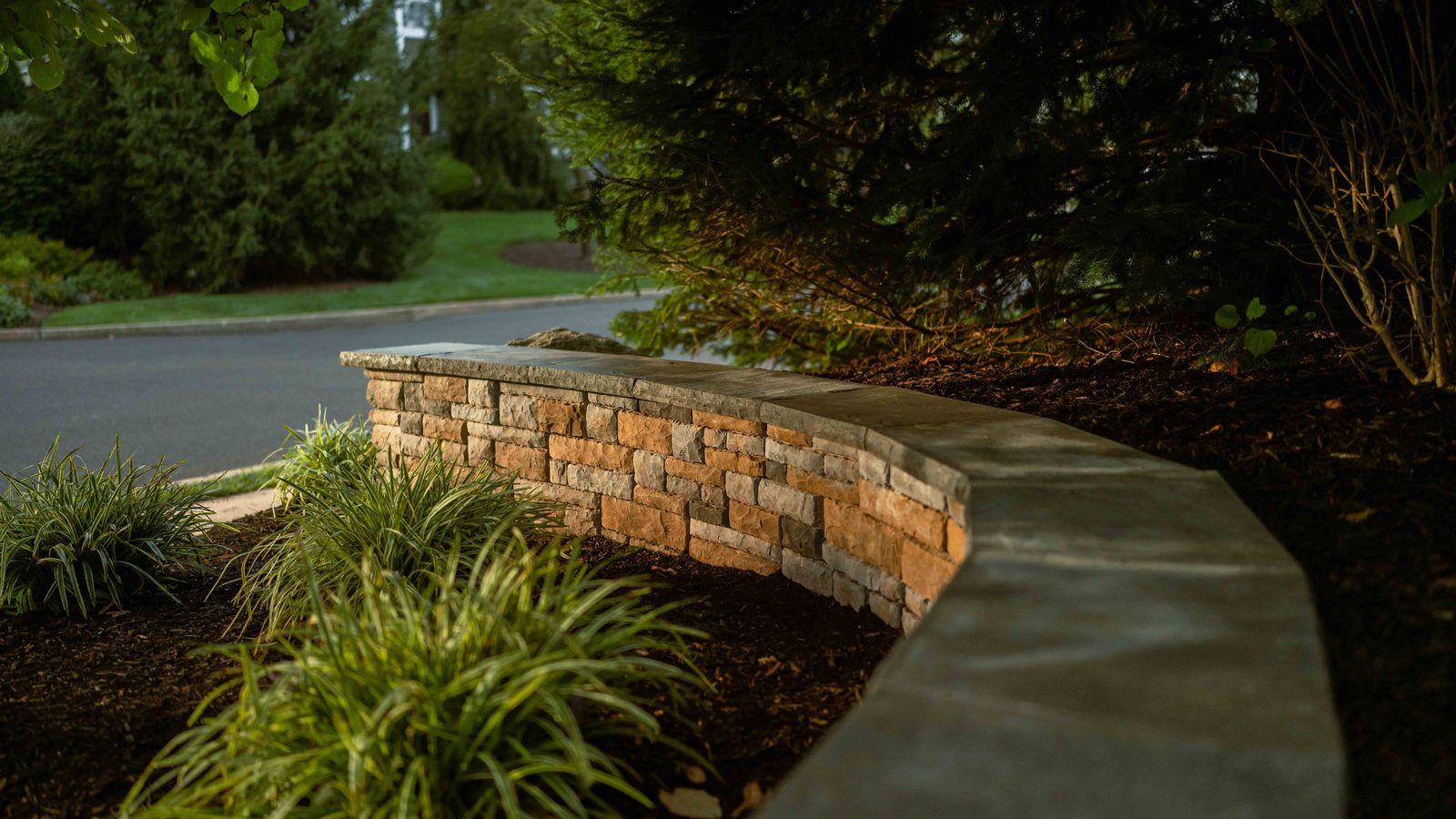 Curved stone retaining wall with landscape lighting by PTB Landscape Management