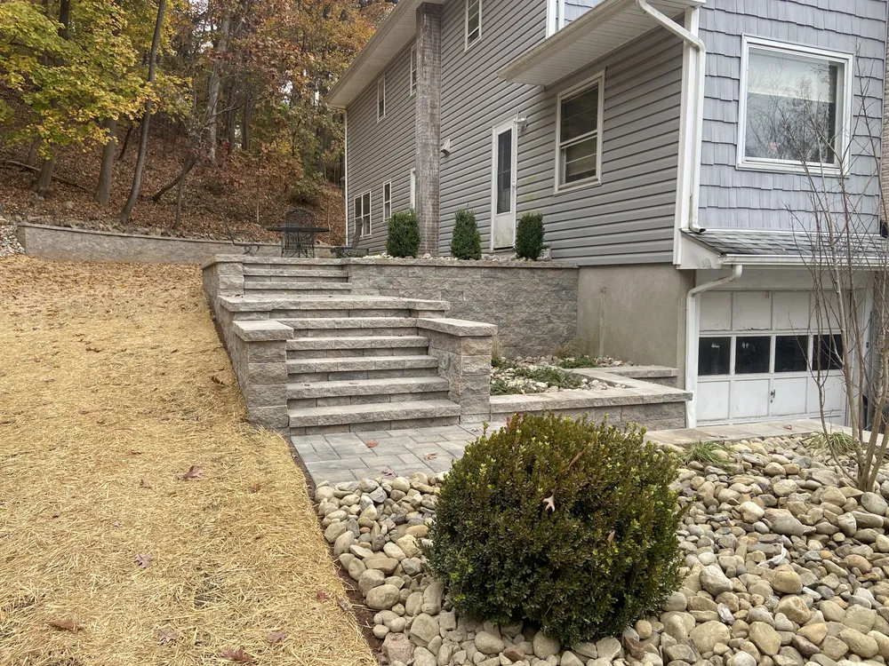 PTB retaining wall with integrated stone steps at a residential property in New Jersey, with landscape drainage stone and plantings